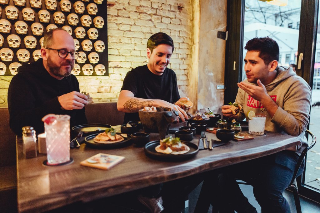Drei Männer sitzen am Tisch und genießen Tacos.