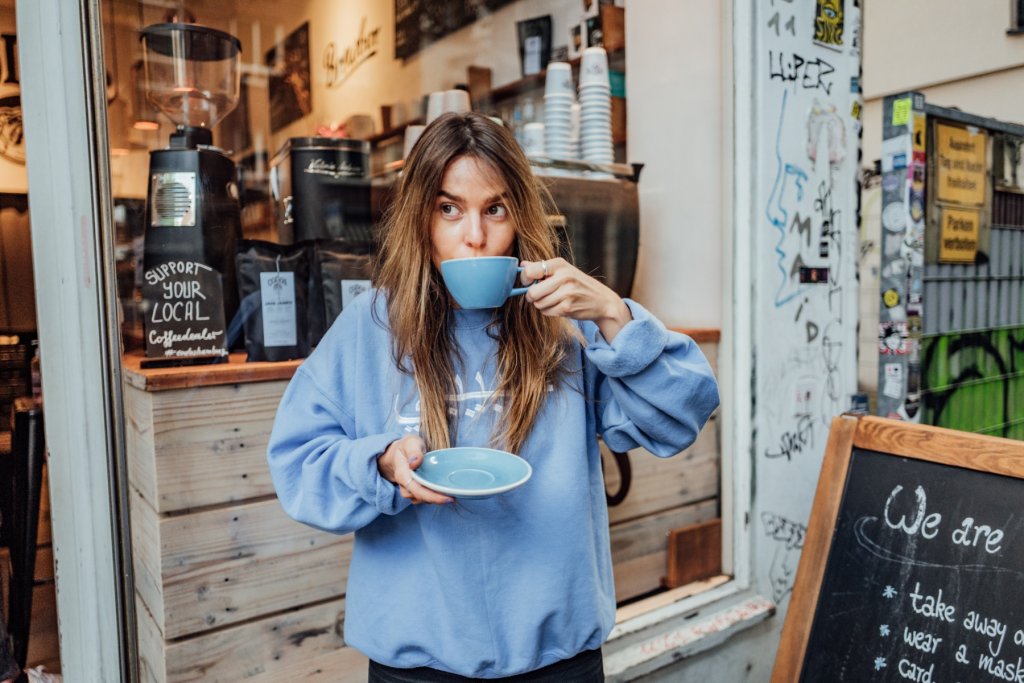 Frau mit blauem Pullover trinkt aus blauer Tasse Kaffee
