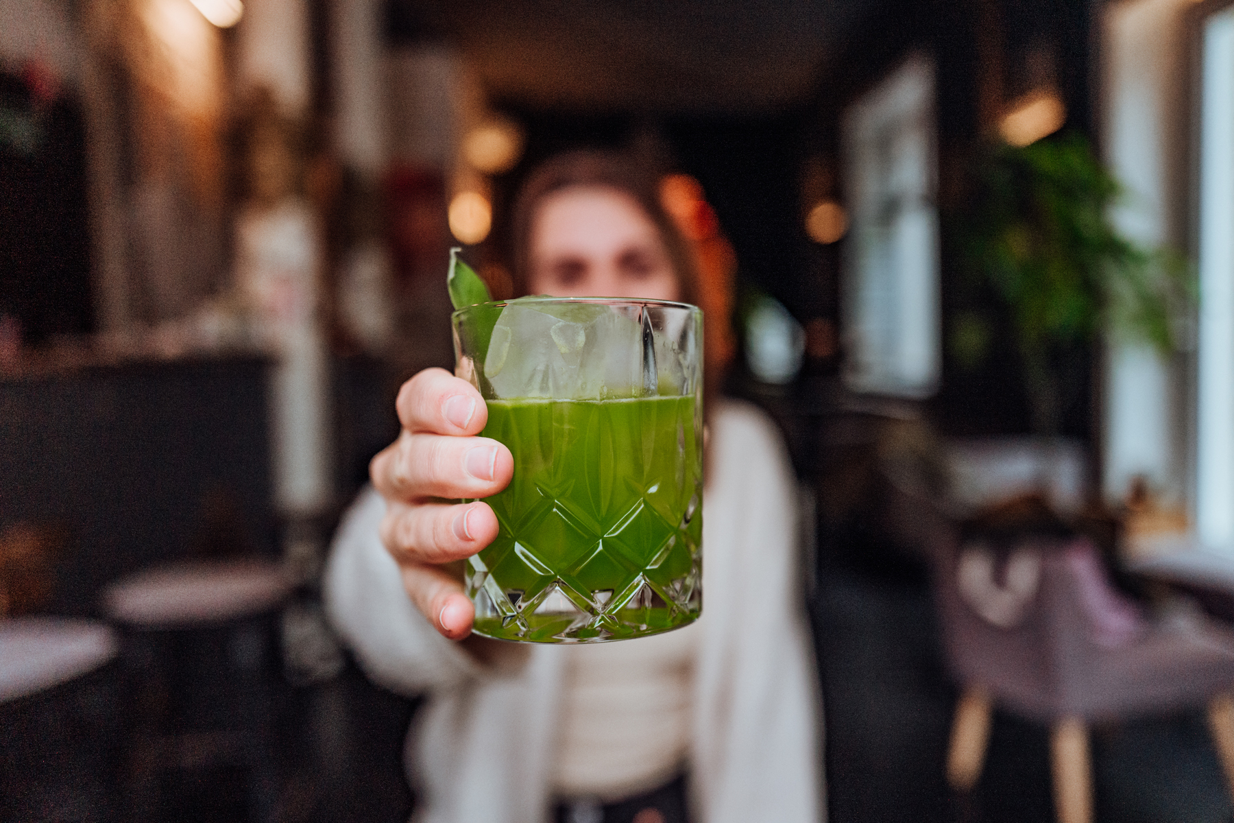 Frau hält grünen Drink mit Basilikum garniert